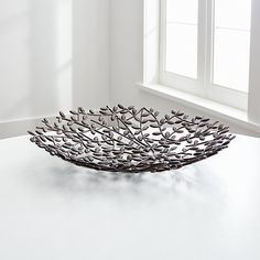 a metal bowl sitting on top of a white table next to a window with sunlight coming in