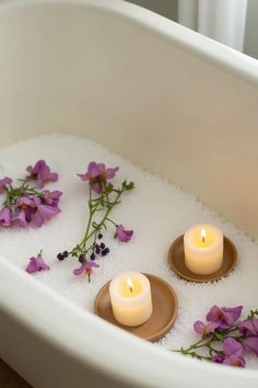 two candles sitting in a bathtub filled with water and purple flowers on the side