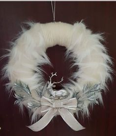 a white wreath hanging from the side of a door with feathers and bows on it