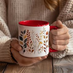 a woman holding a red and white coffee mug with leaves on the inside, in front of her