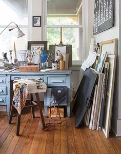 a desk with lots of clutter on top of it in front of a window