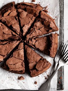 a chocolate cake is cut into slices on a piece of parchment paper next to a knife and fork