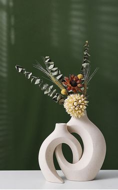 a white vase with flowers in it sitting on a table