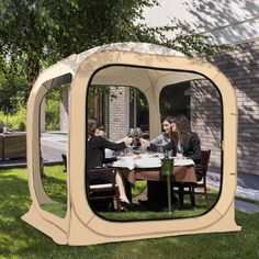 a group of people sitting at a table in a small outdoor tent on the grass