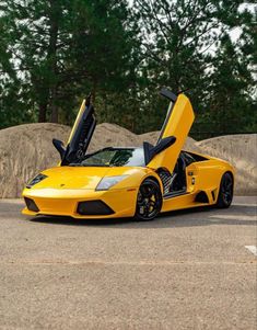 a yellow sports car with open doors parked in a parking lot next to some trees