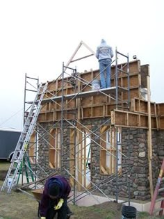 two men working on the roof of a house under construction with scaffolding and ladders