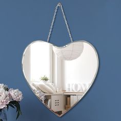 a heart shaped mirror hanging on a wall next to a vase with flowers in it