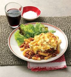 a white plate topped with lasagna and lettuce next to a glass of wine