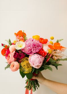 a person holding a bouquet of flowers in their hand with white wall behind them and floor to ceiling