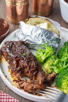 a white plate topped with meat and broccoli covered in bbq sauce next to foil