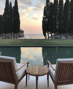 two wooden chairs sitting next to a table on top of a patio near a pool