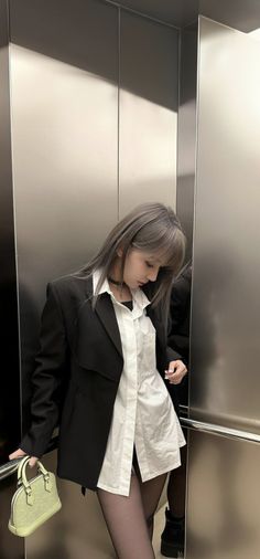 a woman standing in an elevator with her handbag on her hip and looking down