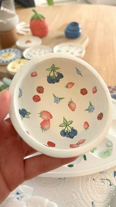 a hand holding a small bowl with strawberries and blueberries on it, in front of plates