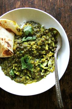 a white bowl filled with green food on top of a wooden table next to a fork