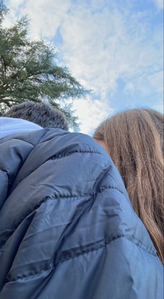 two people standing next to each other under a blue sky with clouds in the background