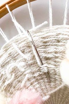 a close up of a needle and thread on a piece of cloth with yarn in the background