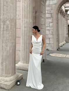 a woman in a white dress standing next to some pillars and looking off into the distance