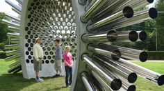 three people are standing in front of a sculpture made out of metal pipes and tubes