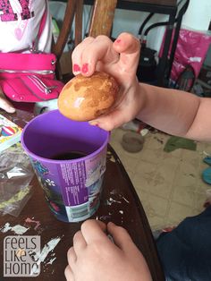 a person holding a doughnut in their hand over a purple cup on a table