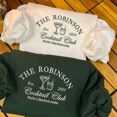 two t - shirts that say the robinsons and cocktail club sitting on a wooden floor