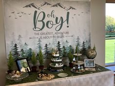 the dessert table is set up for a baby's first birthday party with trees and mountains on it