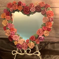 a heart shaped mirror decorated with flowers on top of a wooden table next to a black cloth