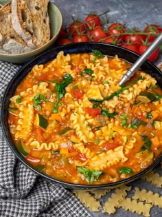 a bowl of pasta soup with bread and tomatoes