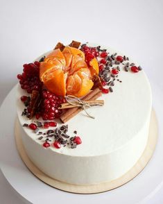 a white cake topped with orange slices and pomegranates next to cinnamon sticks