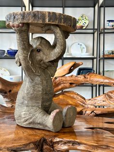 an elephant figurine sitting on top of a wooden table holding a piece of wood