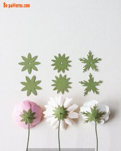 four paper flowers are arranged on a white surface, one is pink and the other is green