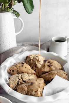 some cookies with icing in a white bowl next to a coffee cup and potted plant