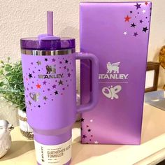 a purple travel mug sitting on top of a table next to a box