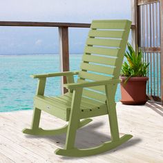 a green rocking chair sitting on top of a wooden deck next to the ocean with potted plants