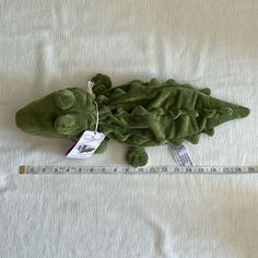 a stuffed alligator laying on top of a bed next to a measuring tape