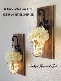 two mason jars with lights and flowers in them are hanging on the wall next to each other