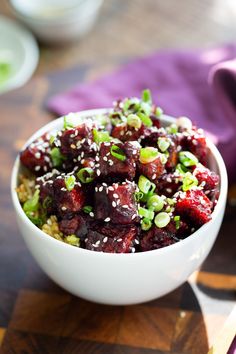 a white bowl filled with food sitting on top of a wooden table next to purple napkins