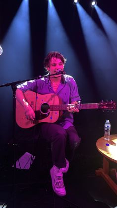 a man sitting in front of a microphone while holding a guitar and singing into a microphone