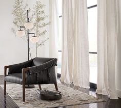 a black leather chair sitting in front of a window next to a lamp and rug