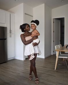 a woman holding a small child in her arms while standing on the floor next to a table