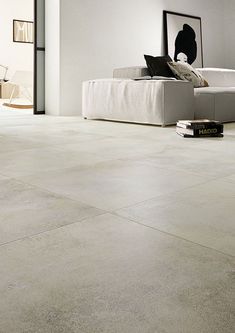 a living room with white walls and flooring that looks like cement tiles, is shown in the foreground