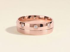 a rose gold wedding band with three princess cut diamonds on the inside and outside of it