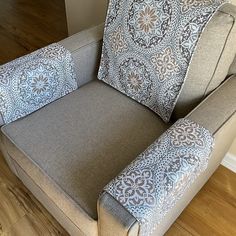 a gray chair with blue and white pillows on it's arm rests against a wall