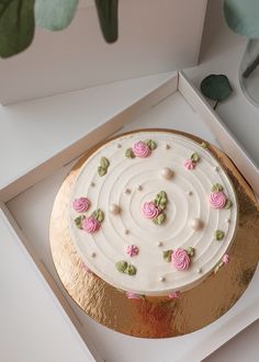 a white cake with pink roses on it in a box next to a plant and other items