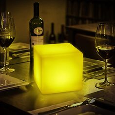 a table with wine glasses and a light up block on top of it next to a bottle of wine