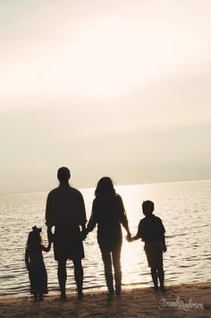 a family walking on the beach holding hands and looking out at the water in silhouette