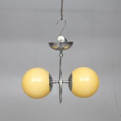 two yellow balls are hanging from a metal fixture with one light on top and the other off