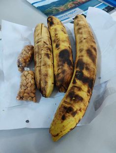 three ripe bananas sitting on top of a piece of paper next to nuts and other items