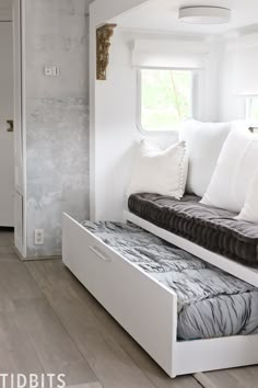 a white couch with pillows on it in front of a window and wooden flooring