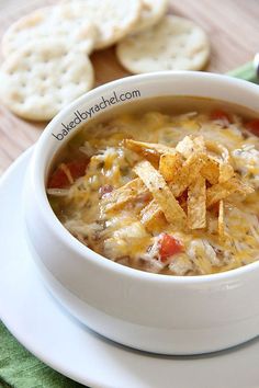 a close up of a bowl of soup with cheese and tortilla chips on the side