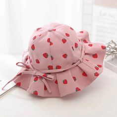 a pink hat with strawberries on it sitting on top of a white table next to a window